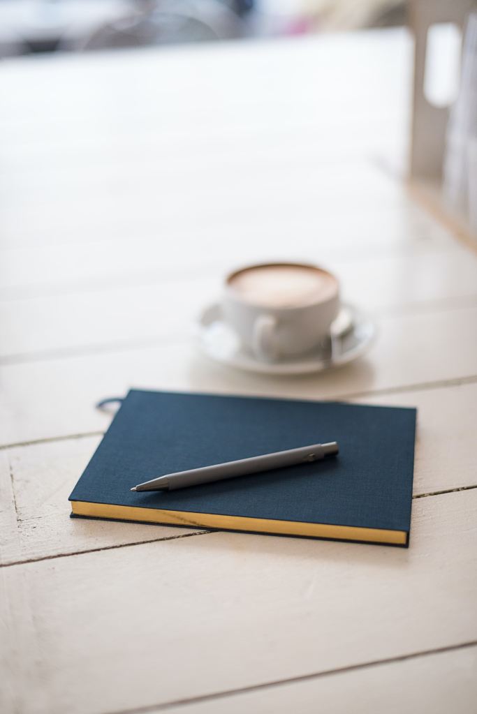 Cup of coffee and a blue notebook and pen.
